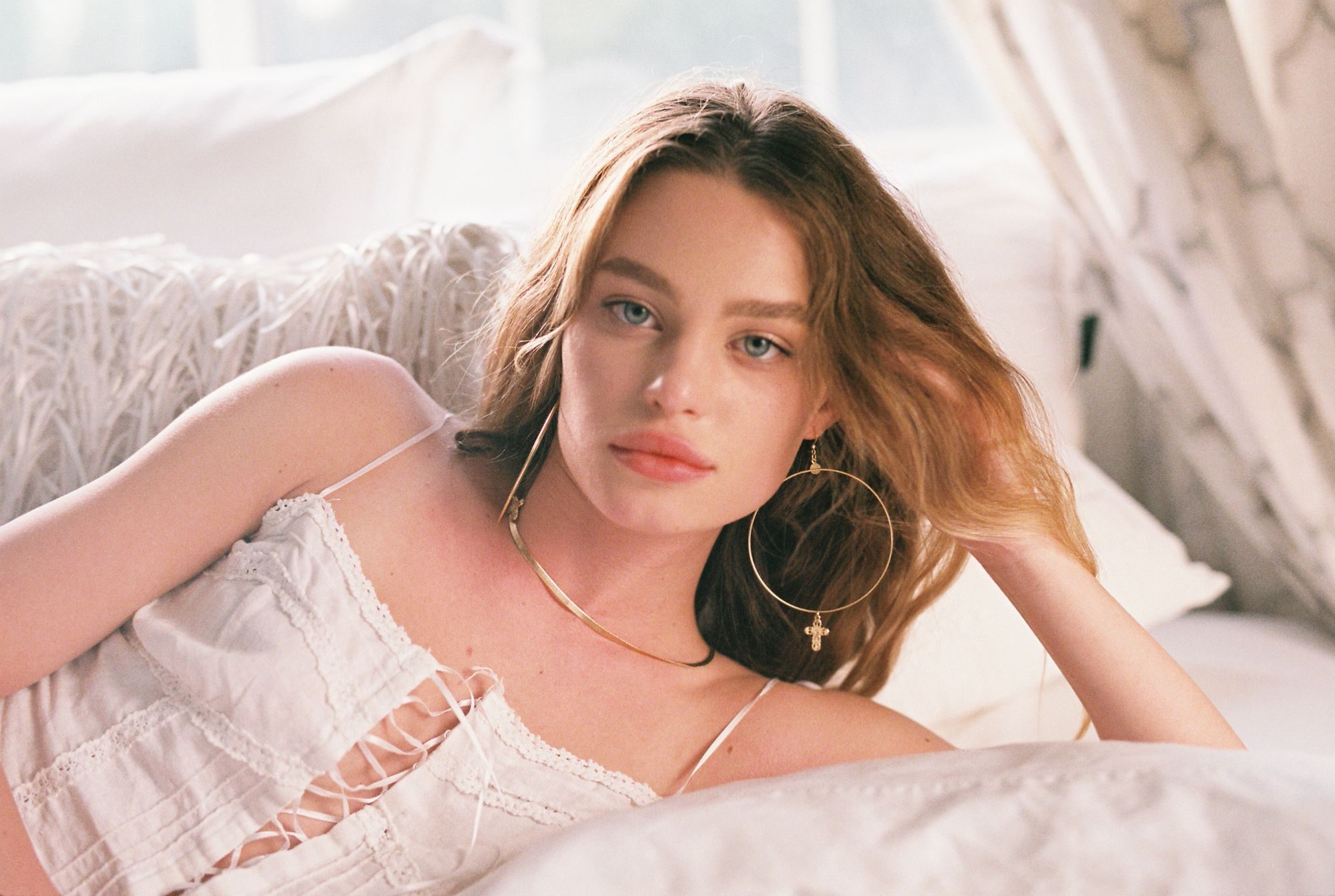 35mm film portrait of a model lounging in white wearing large gold hoop earrings and a herringbone chain