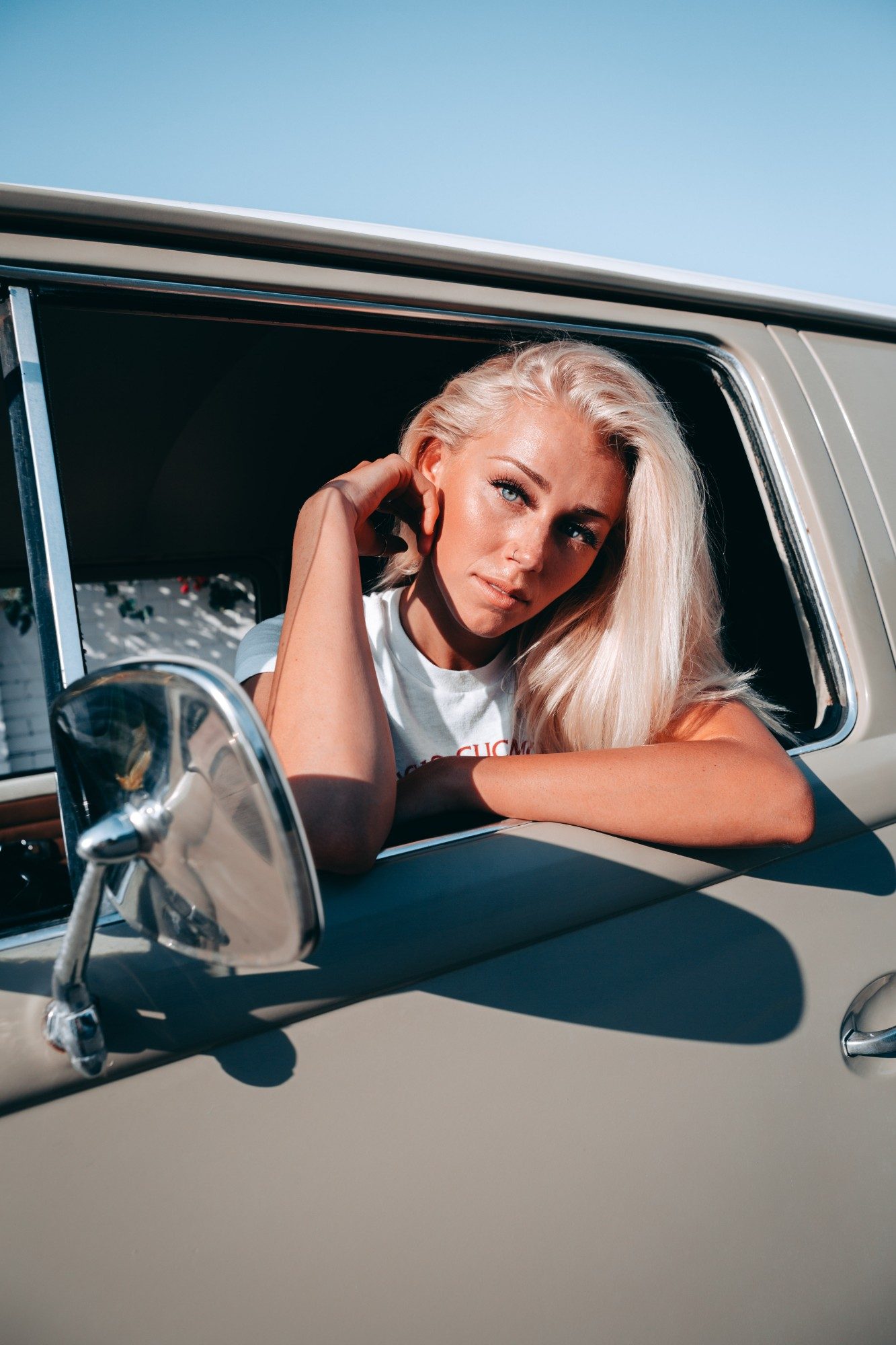 Model leaning out of a vintage VW bus window in a white tee
